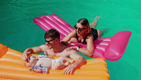 caucasian parents spending time in the pool with their baby. infant lies on the mattress waving feet and hands.