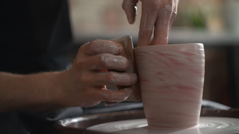 person shaping a ceramic mug on a pottery wheel