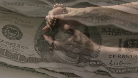 animation of usa banknotes over hands holding rosary