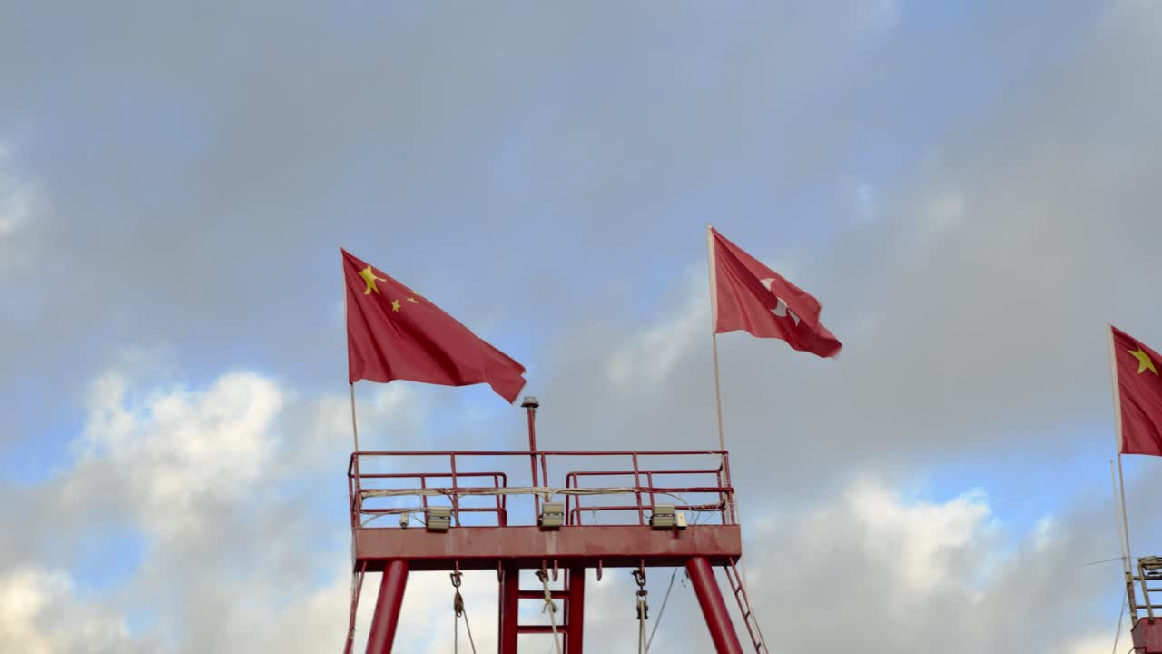 Three Chinese Flags Waving on a Tower Under a Cloudy Sky