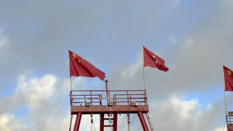 three chinese flags waving on a tower under a cloudy sky