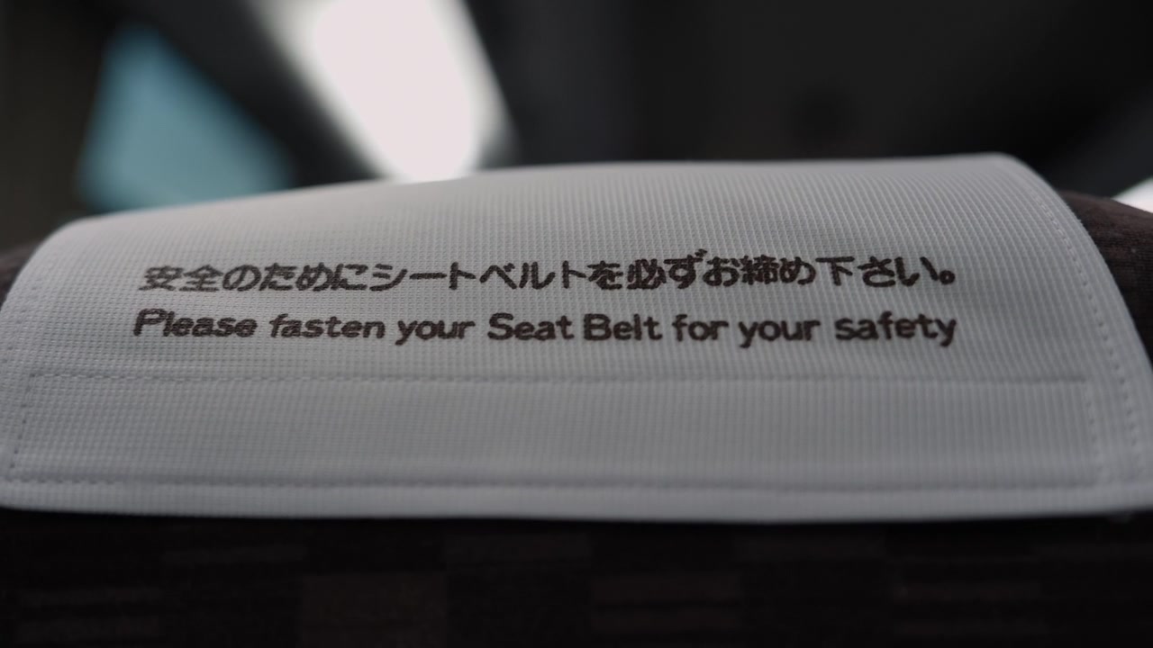 Closeup of white headrest cover with bilingual seat belt safety message on Japanese train seat