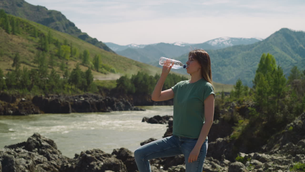 mujer sedienta bebe agua mineral en la orilla del río de la montaña