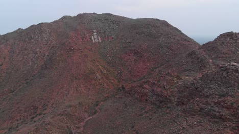 Aerial-fly-in-toward-symbol-in-white-on-red-rocky-mountainside,-Mongolia