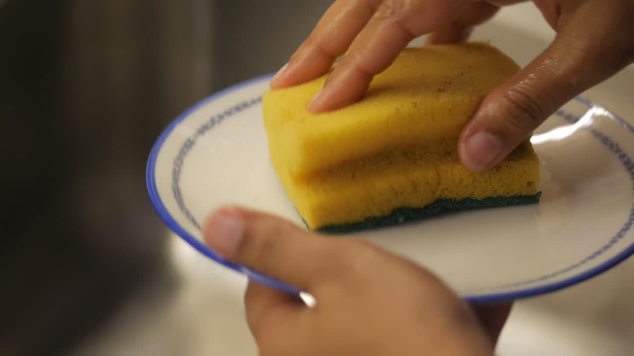 Hands washing a plate with a sponge