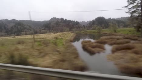 Driving-by-a-river-coming-from-tree-covered-mountains-in-Oregon