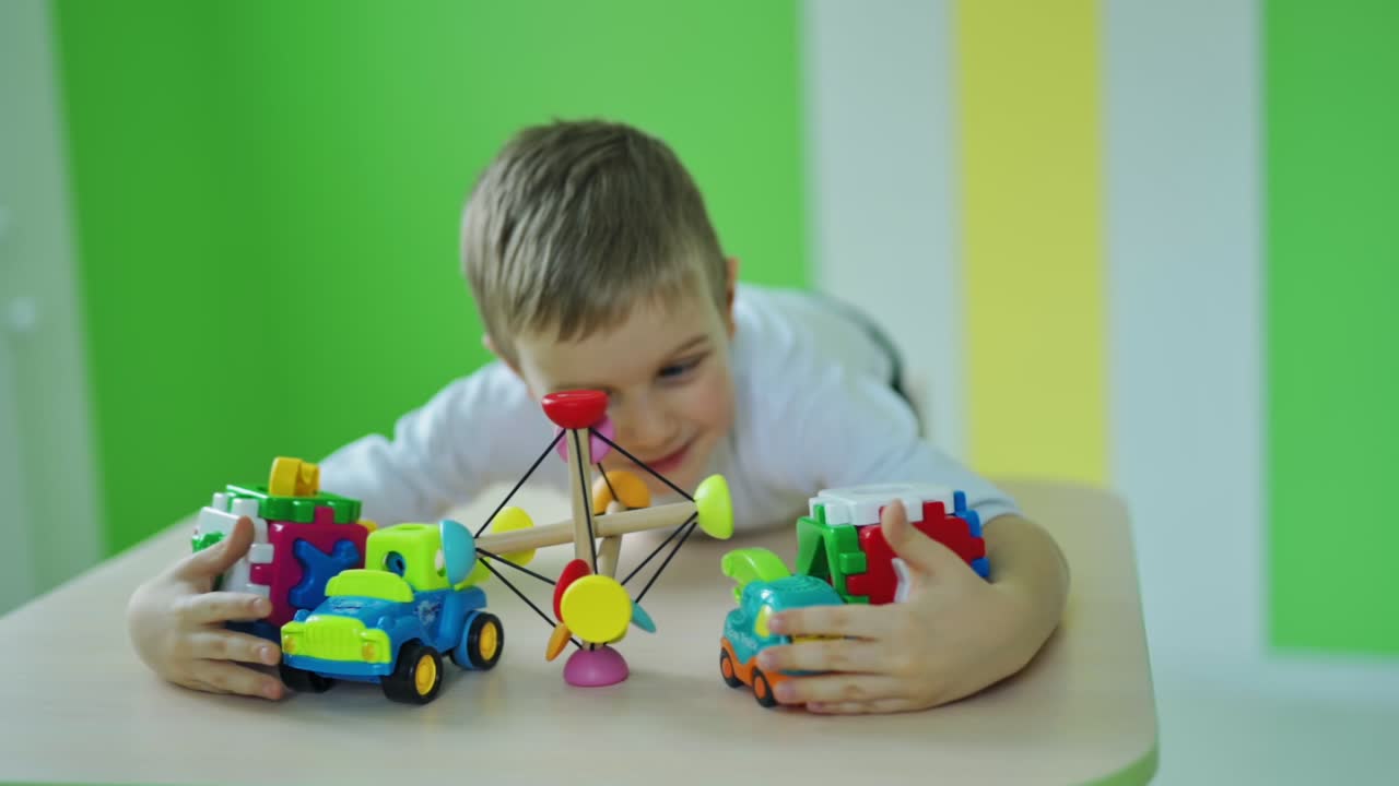 Happy little boy with toys.Bright toys on the table. Cute child is captures all plastic toys on the colorful room background. Slow motion.