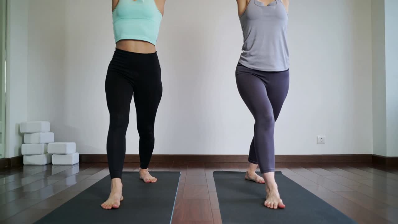 Two women doing yoga on mats, hands on mat starting lift into single-leg balance for stability