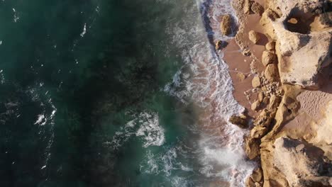 aerial shot of ocean waves crashing on rocks on a warm summer day