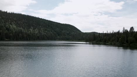 Overflying-The-Calm-Water-Of-The-Lost-Lake-With-Lush-Green-Forest-On-The-Mountains-In-Gaspesie-Peninsula,-Quebec,-Canada