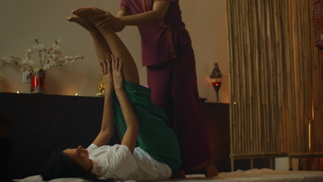 Asian-Woman-performs-Traditional-Thai-Massage-to-beautiful-European-Woman.-Rehabilitation-and-Treatment-after-Injuries-with-the-help-of-Massage.-Relax-and-Rest-from-massage-of-Legs-Arms-and-Back.-Therapeutic-massage