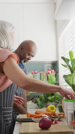 vertical video of happy diverse senior couple preparing food and composting vegetables in kitchen