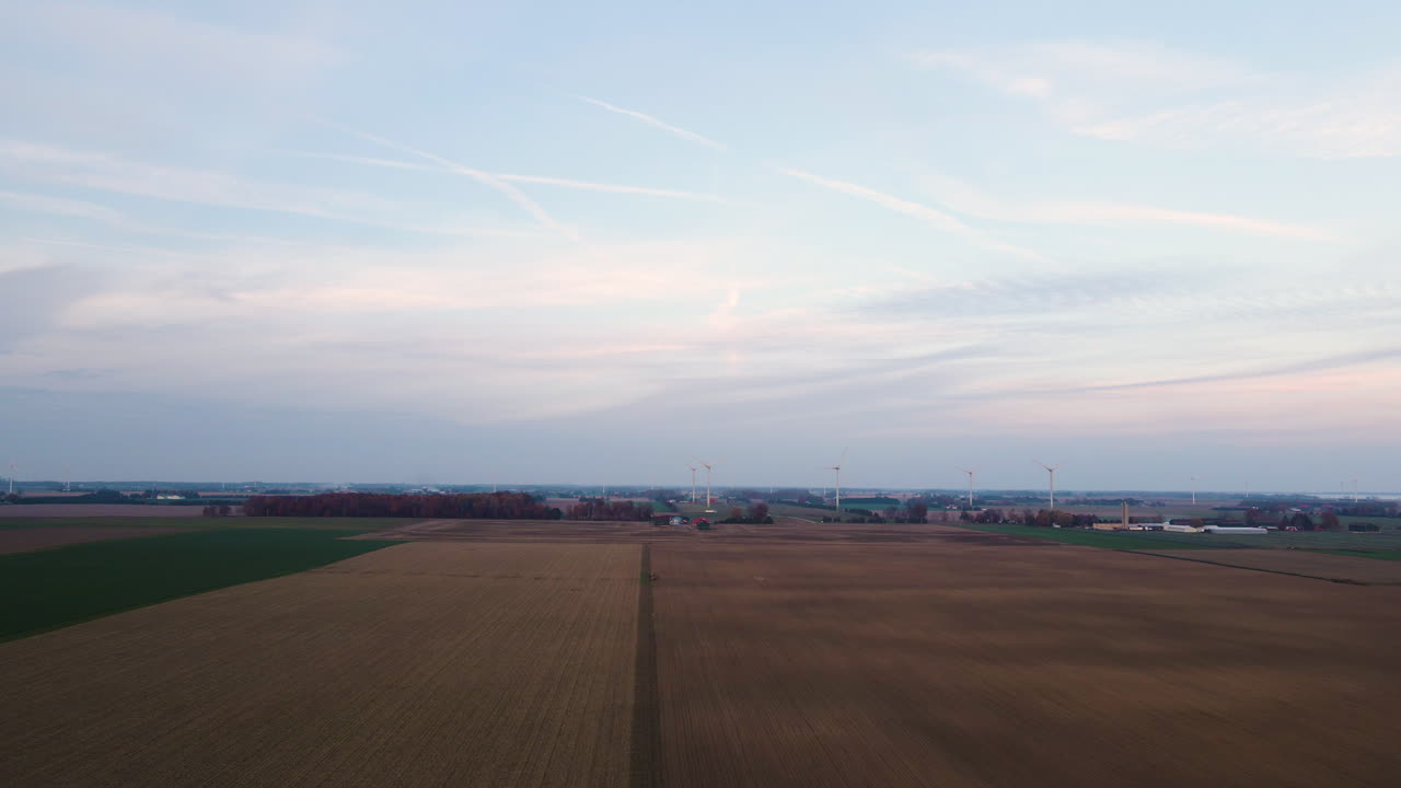 Panoramisk luftfoto over landbrugsmarker med vindmøller i det fjerne på en overskyet dag