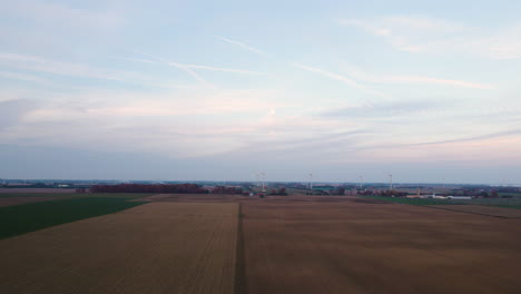 Antena-Panorámica-Sobre-Campos-Agrícolas-Con-Turbinas-En-La-Distancia,-Día-Nublado