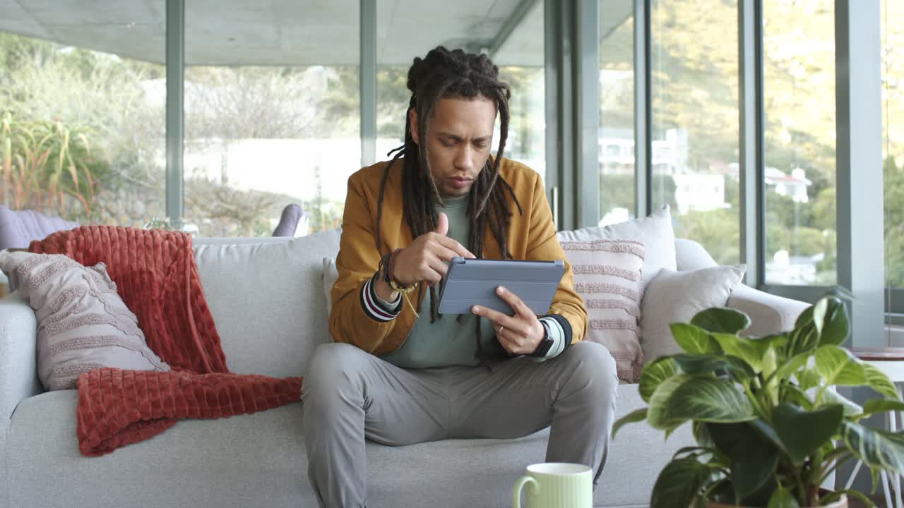 Man in his thirties powering on tablet, unlocking, scrolling on couch at home for remote work