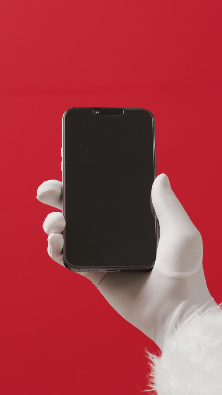 video vertical de la mano de santa claus con teléfono inteligente sobre fondo rojo