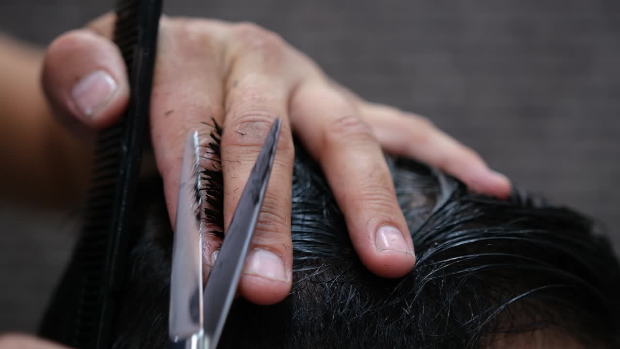 primer plano de un peluquero cortando el pelo de un hombre con peine y tijeras.