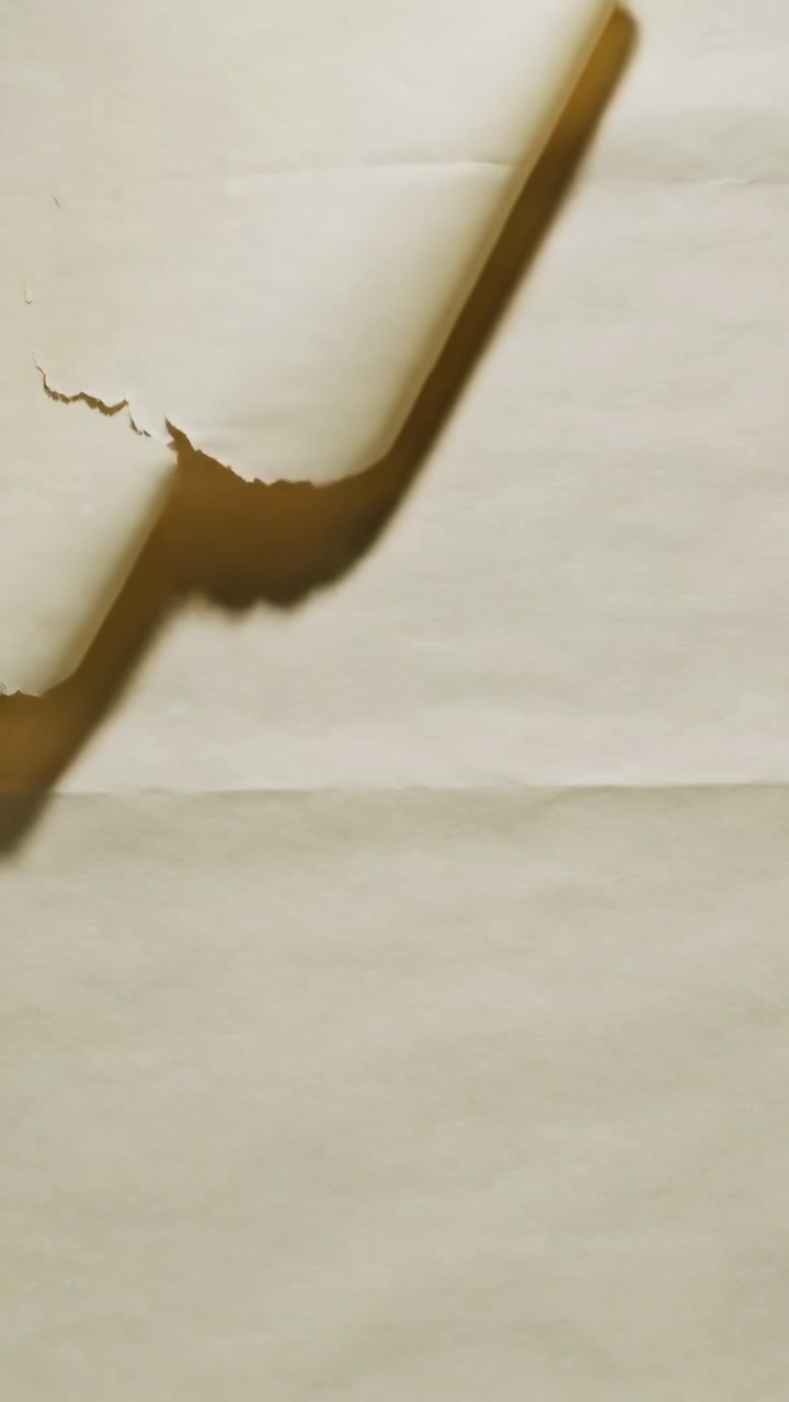Vertical video: Peeling curled torn margin sweeping across cream sheet, revealing crack lines