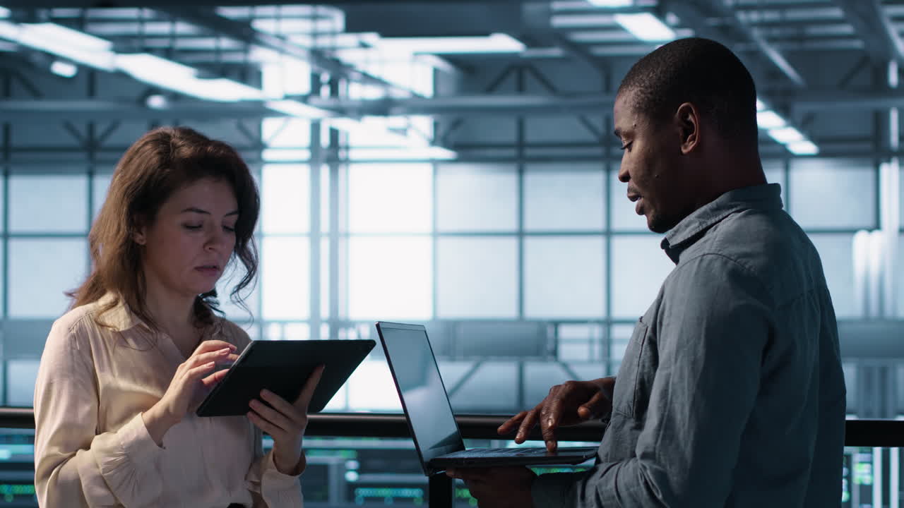 Smiling admins using laptop in data center, managing server virtualization