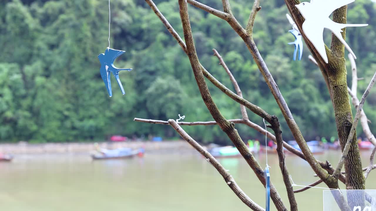Blue mobile hanging from branches near river and boats