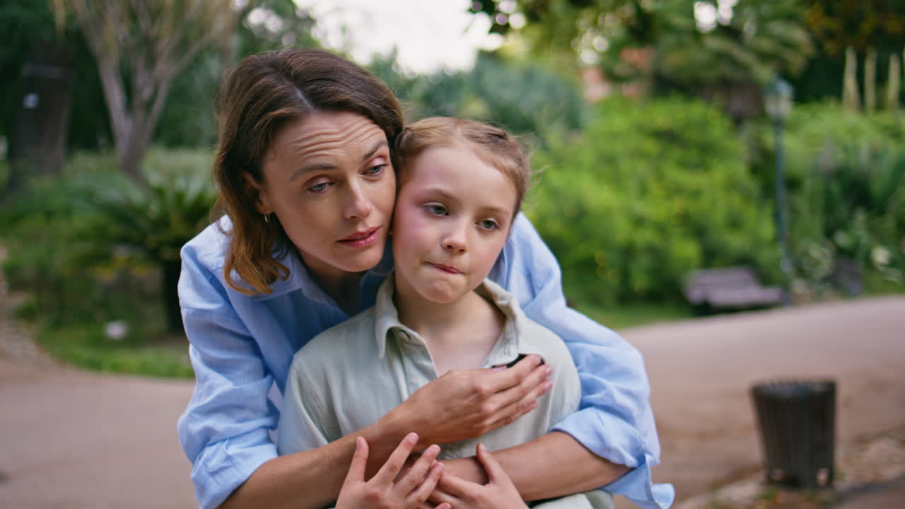 Tender mother daughter embracing at park looking closeup. Woman pointing finger