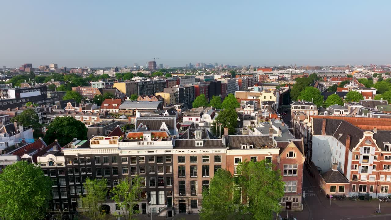 Stunning drone view of Amsterdam’s canal lined with boats, bridges, and historic Dutch houses under clear skies