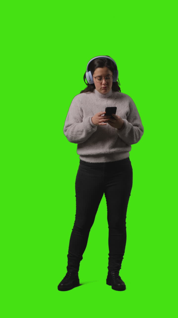 video vertical de larga duración de una mujer con auriculares inalámbricos transmitiendo música desde un teléfono móvil contra la pantalla verde 2