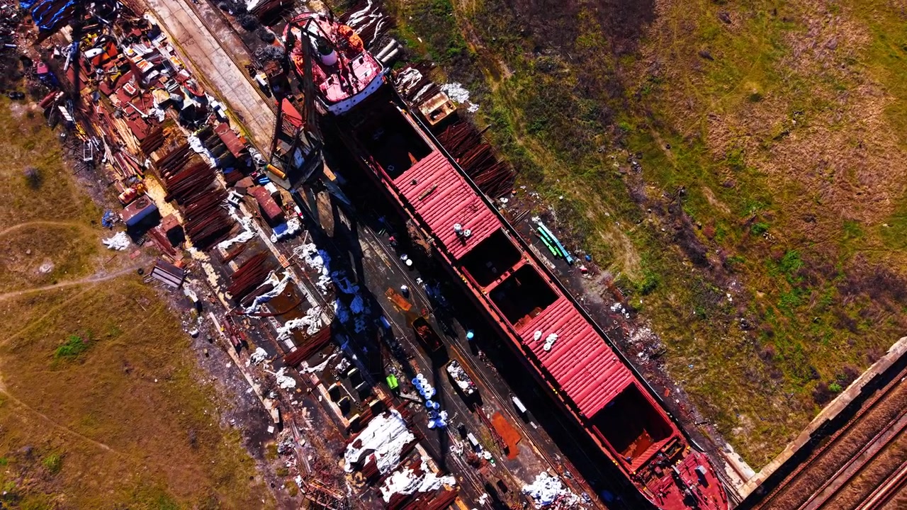 Vista da drone di una nave da carico in riparazione. Scafo della nave posizionato su binari del cantiere navale circondato da rottami metallici.