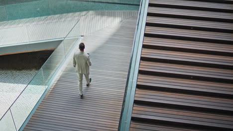 calm businessman crossing ramp holding smartphone back view. man walking down