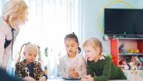 neugierige grundschüler und ihre lehrerin. kleine mädchen an einem runden tisch arbeiten zusammen mit dem pädagogen im klassenzimmer.