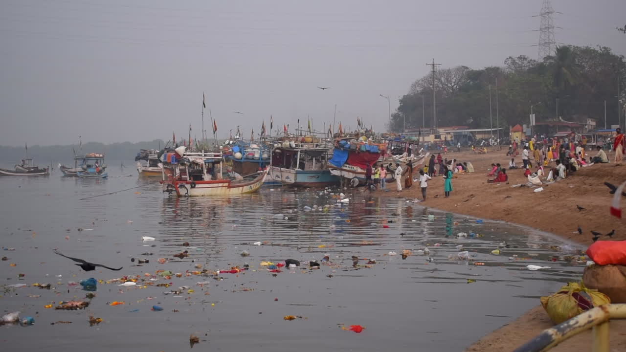 Water pollution near a sea shore,flowers, plastics,food,bottles and waste in Mumbai city, India, near a small fishing boats docked or parked on shore video background in prores 422 HQ