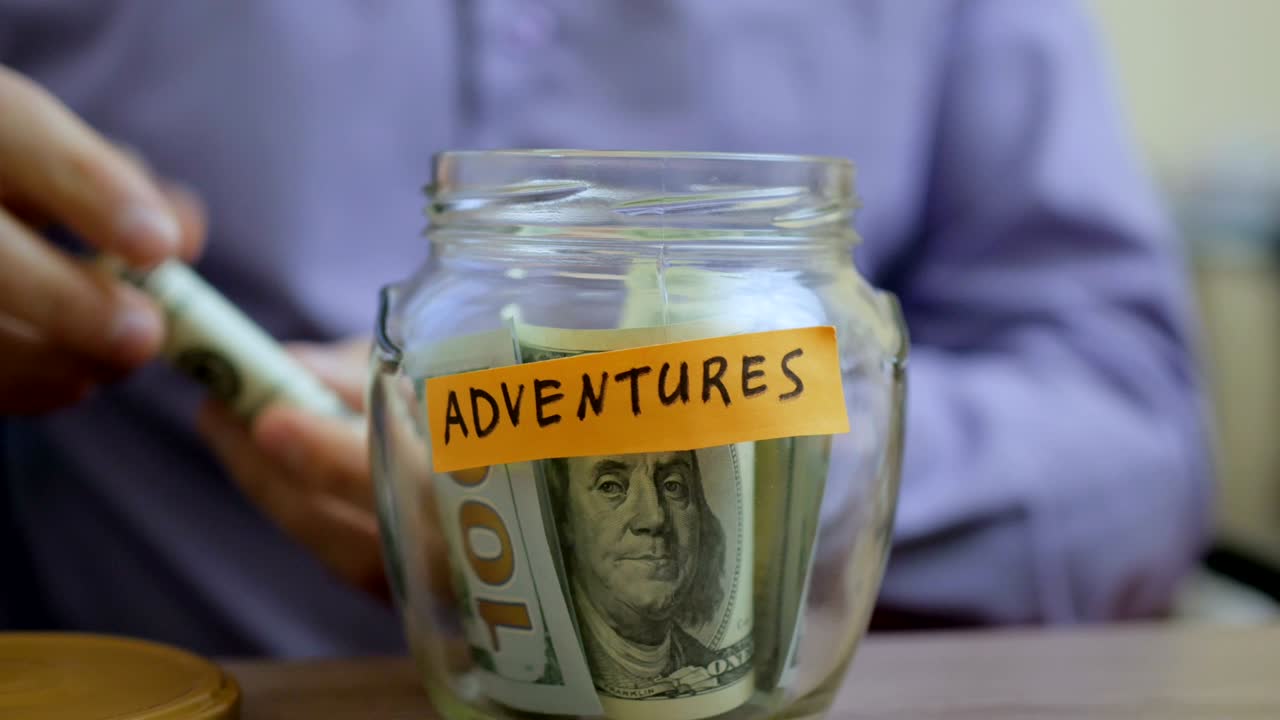 hombre caucásico poniendo un frasco de vidrio puesto en una mesa de cajón con sus ahorros para futuras aventuras