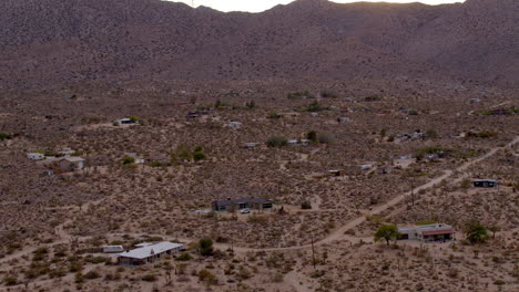 antena sobre camino de tierra y casas pequeñas en el desierto de joshua tree, california con un auto en un camino de tierra