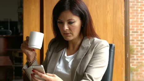 business woman using her smartphone while drinking coffee