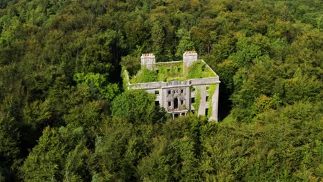 aerial orbit of moore hall ruins hidden in mayo forest on a sunny day