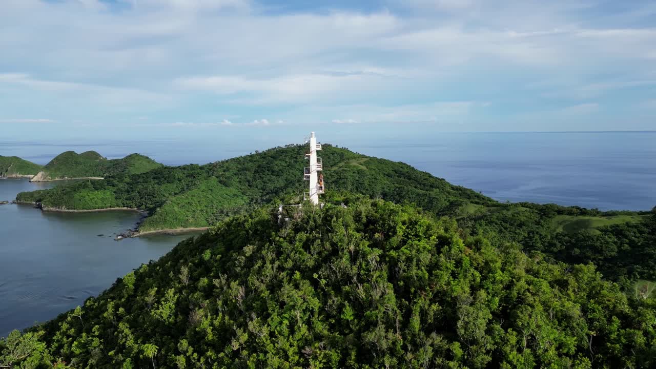 맑은 바닷물과 정글을 배경으로 무성한 섬 잎 위에 있는 하얀 등대의 공중 궤도 전망