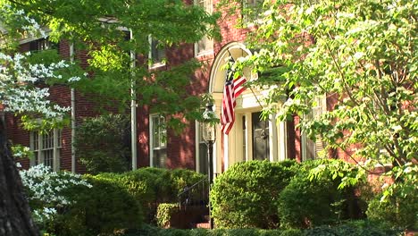 Eine-Amerikanische-Flagge,-Die-Durch-Die-Bäume-Hindurch-Zu-Sehen-Ist,-Hängt-Stolz-Neben-Einer-Haustür