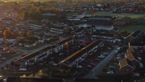 UK-Townhouse-estate-aerial-rising-view-with-early-morning-sunrise-light-leaks-over-Autumn-coloured-trees-and-rooftops