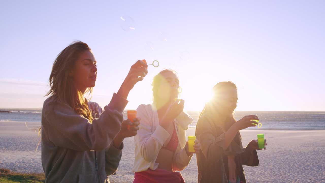 해가 지면 해변에서 거품을  ⁇ 는 여자 친구들이 느린 동작을 하고 있습니다.