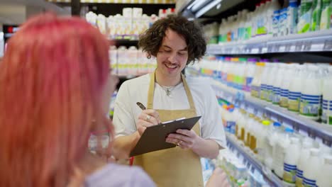 Over-the-shoulder-a-girl-with-pink-hair-points-to-a-guy-supermarket-worker-while-taking-inventory-together-in-a-supermarket