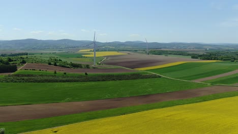 Pristine-rolling-green-grey-and-yellow-farm-fields-with-windmill-turbine-spinning