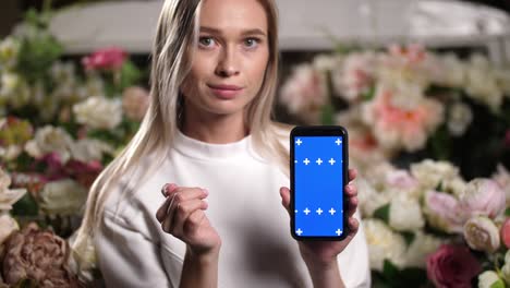 portraits of smiling woman looking at camera with blue screen phone in hands.