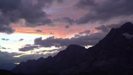 vibrant orange and pink hues light up textured morning clouds over the jagged silhouettes of swiss mountains. location: swiss alps, switzerland (schweiz).