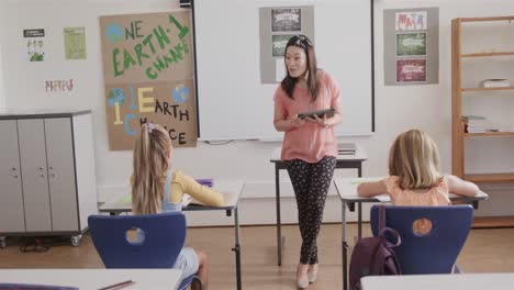 happy diverse female teacher with tablet and girls at desks in elementary school class, slow motion