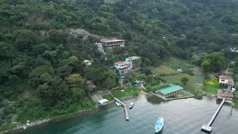 Drone-view-in-Guatemala-showing-a-hotel-on-a-green-hill-facing-a-blue-lake-on-a-cloudy-day-in-Atitlan