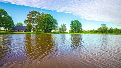 Hermoso-Timelapse-Matutino-A-Través-De-Un-Lago-Con-Luz-Solar-Iluminando-El-Albergue-Ubicado-Entre-árboles-Verdes-En-Letonia