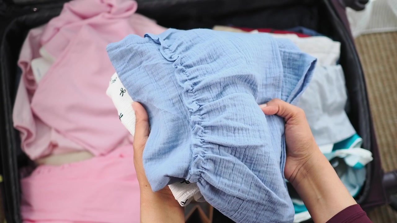 Person Packing Baby Clothes into a Suitcase