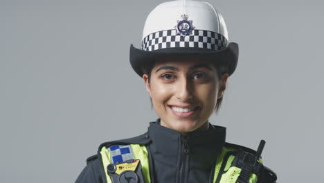 Retrato-De-Estudio-De-Una-Joven-Y-Sonriente-Oficial-De-Policía-Sosteniendo-Un-Casco-Contra-Un-Fondo-Liso