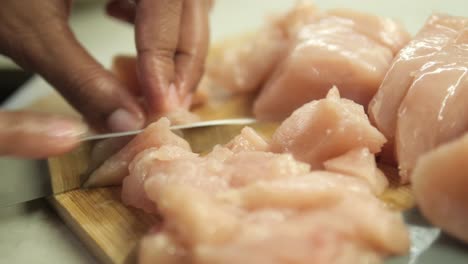 cerca de las manos cortando pollo en una tabla de cortar