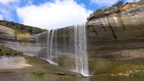 Toma-Estática-De-Cascadas-De-Mangatiti-Que-Fluyen-Desde-Un-Acantilado-Rocoso-Contra-El-Cielo-Azul-Y-Las-Nubes